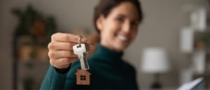 Smiling new homeowner posing by holding out her housekeys in front of her