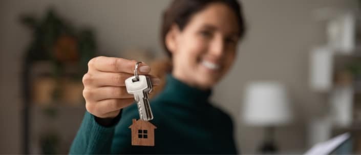Smiling new homeowner posing by holding out her housekeys in front of her